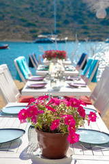 View of restaurant or cafe and bougainvillea flowers on beach in Gumusluk, Bodrum city of Turkey. Aegean seaside style colorful chairs, tables and flowers in Bodrum town near beautiful Aegean Sea.