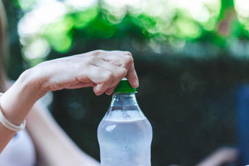 Young hand opens transparent bottle with ice cold water on a hot summer day – Person holding a plastic recipient with cool healthy beverage outdoor on a green scenery