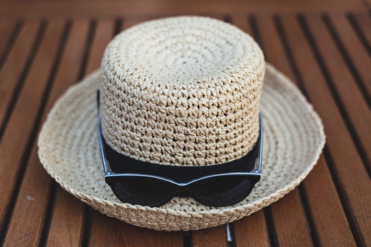 Yellow straw hat with ribbon and black sunglasses placed on a wooden table outdoor – Basic summer accessories used for protection against heat and bright sunlight