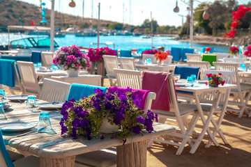View of restaurant or cafe and bougainvillea flowers on beach in Gumusluk, Bodrum city of Turkey. Aegean seaside style colorful chairs, tables and flowers in Bodrum town near beautiful Aegean Sea.