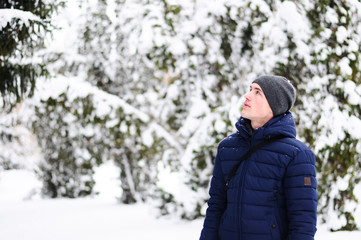 Fashion portrait in winter day over snowy trees forest background, empty copy space. Man look up left side