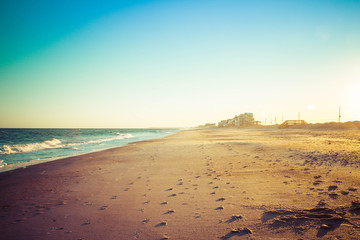 Foot prints in the sand leading away form the viewer on a long sandy beach in evening light.