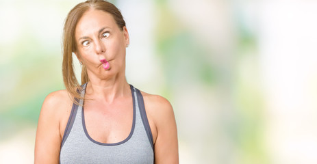 Fototapeta na wymiar Beautiful middle age woman wearing sport clothes over isolated background making fish face with lips, crazy and comical gesture. Funny expression.