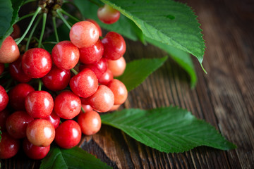 Cherry fresh red berries, and green leaves on a wooden background