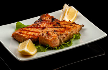 Grilled trout with lemon on a platter on a black table