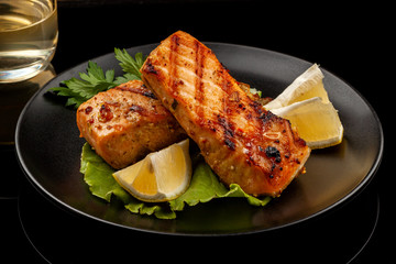 Grilled trout with lemon on a platter on a black table