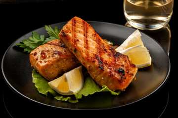 Grilled trout with lemon on a platter on a black table