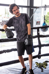 Fototapeta na wymiar hombre sentado en esquina de ring de box en gimnasio entrenando con guantes rojos y sacos de entrenamiento