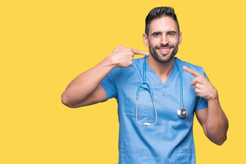 Handsome young doctor surgeon man over isolated background smiling confident showing and pointing with fingers teeth and mouth. Health concept.