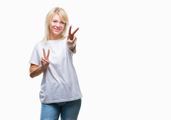 Obraz premium Young beautiful blonde woman wearing white t-shirt over isolated background smiling looking to the camera showing fingers doing victory sign. Number two.