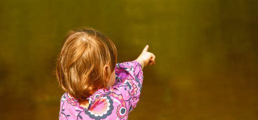 Little cute child girl  relaxing in nature at the lake and pointing with finger somewhere far away....