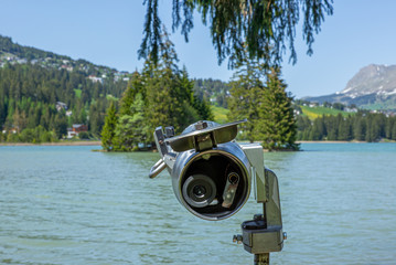 A telescope with view of the Swiss Alps on the shore of a lake in Summer