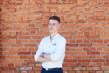 Portrait of a casually dressed young businessman standing with his arms crossed against a brick wall