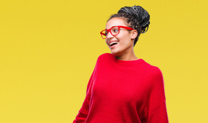 Young braided hair african american girl wearing sweater and glasses over isolated background looking away to side with smile on face, natural expression. Laughing confident.