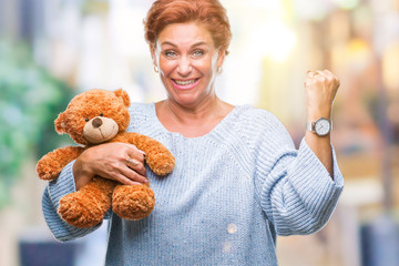 Senior caucasian woman holding teddy bear over isolated background screaming proud and celebrating...