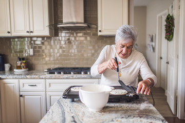 Portrait of senior woman cooking pancakes for breakfast