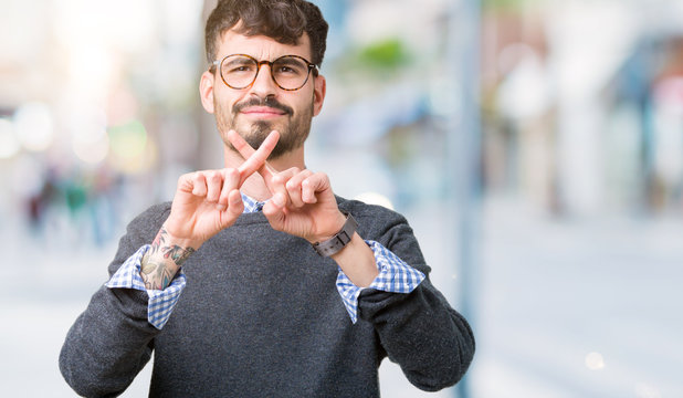 Young handsome smart man wearing glasses over isolated background Rejection expression crossing fingers doing negative sign