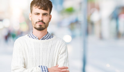 Young handsome man wearing winter sweater over isolated background skeptic and nervous, disapproving expression on face with crossed arms. Negative person.