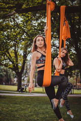 Two pensive beautiful womans are posing for photographer while resting on slings in the summer park.