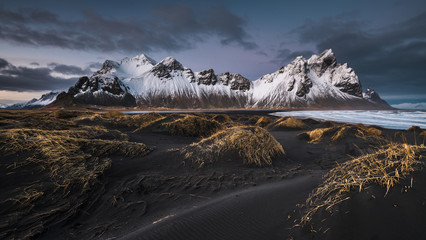 Water near black wild lands and stone mountains in snow
