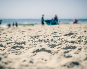 Foreground Sand in Focus, Blurred People with Blanket on Beach