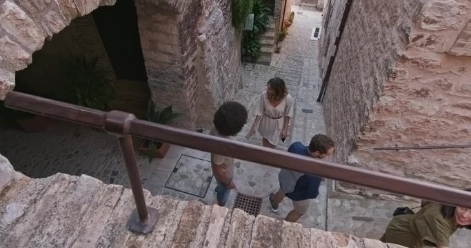 Four happy tourist people walking and running through small street visiting rural town of Spello.Top high view.Friends italian vacation trip in Umbria.4k slow motion
