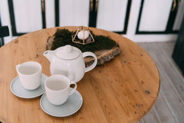 Tea set, white teapot and two cups on saucers on wooden table