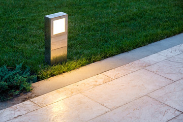 ground lantern lighting marble walkway in the evening park with a green lawn, closeup lantern...