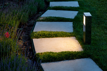 square tile marble path illuminated by a lantern in the backyard, a winding path in the flowerbed...