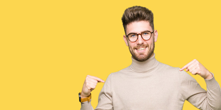 Young handsome business man wearing glasses looking confident with smile on face, pointing oneself with fingers proud and happy.