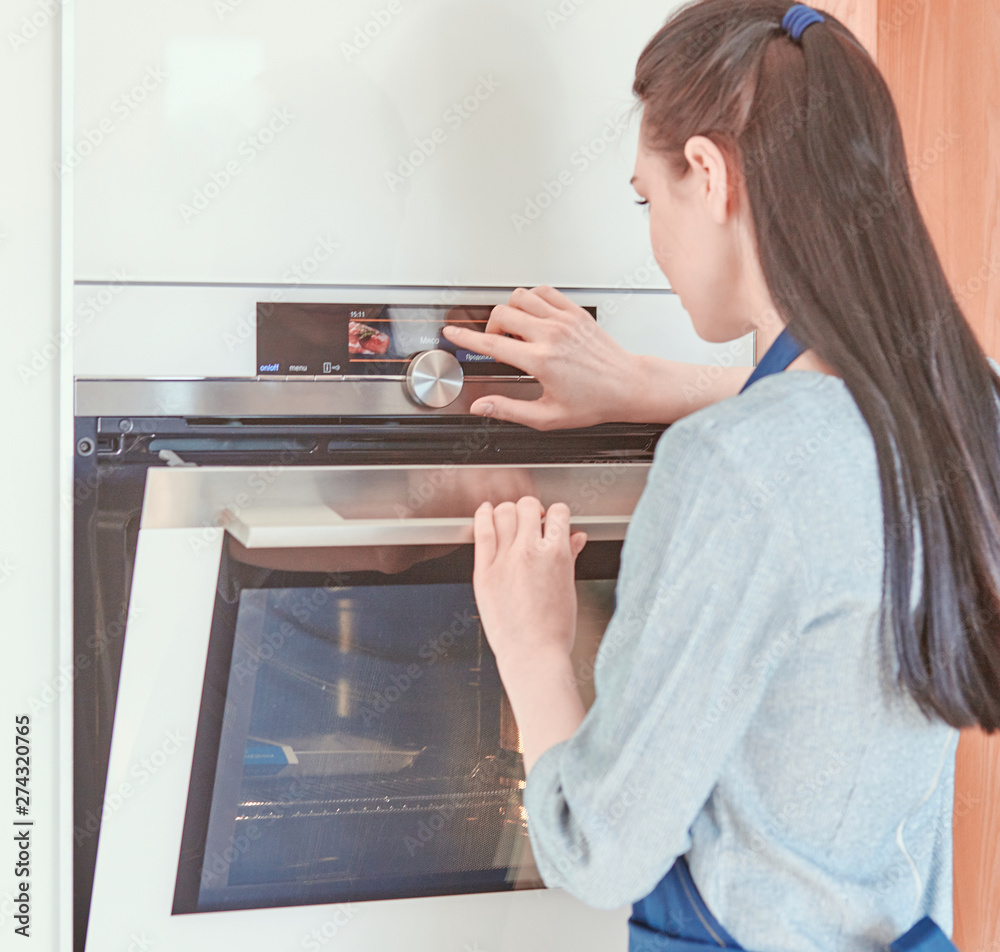 Wall mural beautiful woman in the kitchen, waiting with the front of the oven