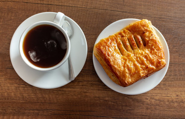 Aerial view of a cup of hot coffee served on a wooden textured coffee table next to a pineapple cake