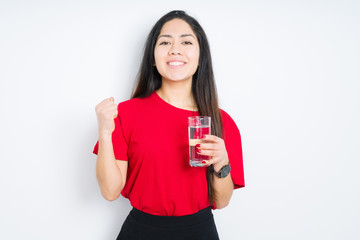 Young brunette woman drinking a glass of water over isolated background screaming proud and celebrating victory and success very excited, cheering emotion