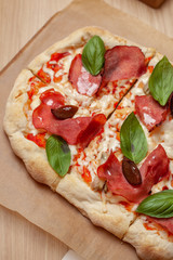 Roman square pizza on a thick dough with mozzarella, pastrami, sweet plum and basil leaves, served on a wooden table