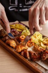Obraz na płótnie Canvas Man is eating shish-kebab, made on coal grill, served with other bbq meat treats, coleslaw and chips on a wooden tray