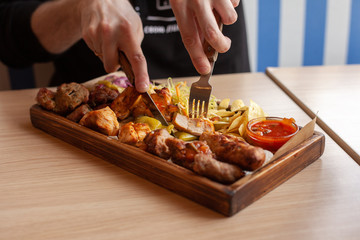Man is eating shish-kebab, made on coal grill, served with other bbq meat treats, coleslaw and chips on a wooden tray