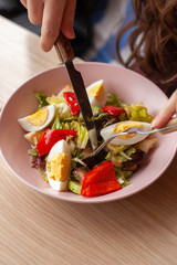 Woman is eating traditional american cobb salad with chopped avocado, tomatoes, hard boiled egg, roasted chicken and greens for a healthy lunch