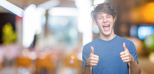 Young handsome man wearing blue t-shirt over isolated background success sign doing positive gesture with hand, thumbs up smiling and happy. Looking at the camera with cheerful expression