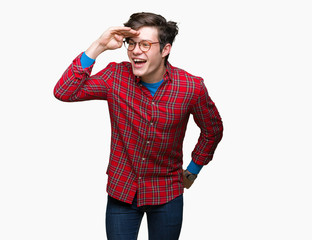 Young handsome man wearing glasses over isolated background very happy and smiling looking far away with hand over head. Searching concept.