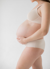 Happy young mother in anticipation of the birth of the baby. A pregnant girl stands clasping her bare stomach with her hands. On a white background.
