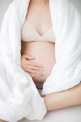 Happy young mother in anticipation of the birth of the baby. A pregnant girl is sitting clasping her bare belly. On a white background.