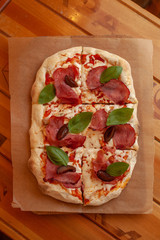 Top view of roman square pizza on a thick dough with mozzarella, pastrami, sweet plum and basil leaves, served on a wooden table