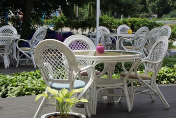 white chairs and a table standing on the street among the green leaves of vegetation