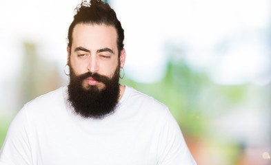 Young hipster man with long hair and beard wearing casual white t-shirt with hand on stomach because indigestion, painful illness feeling unwell. Ache concept.