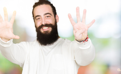 Young man with long hair and beard wearing sporty sweatshirt showing and pointing up with fingers...