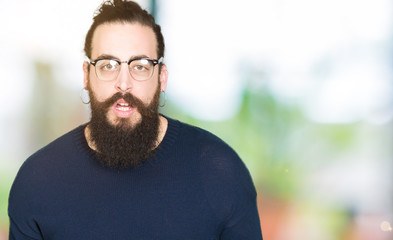 Fototapeta premium Young hipster man with long hair and beard wearing glasses afraid and shocked with surprise expression, fear and excited face.