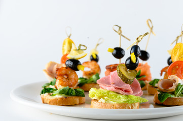 Variety of cold appetizers for party buffet or banquet ? different states canapes on skewers with greens, meat, cheese and seafood isolated on white