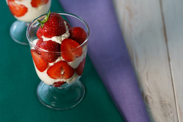 Whipped cream and strawberries served in a glass. Purple and dark green napkins, white wooden table, high resolution
