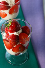 Whipped cream and strawberries served in a glass. Purple and dark green napkins, white wooden table, high resolution