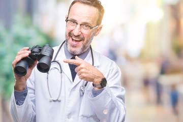 Middle age senior hoary doctor man looking through binoculars isolated background very happy pointing with hand and finger